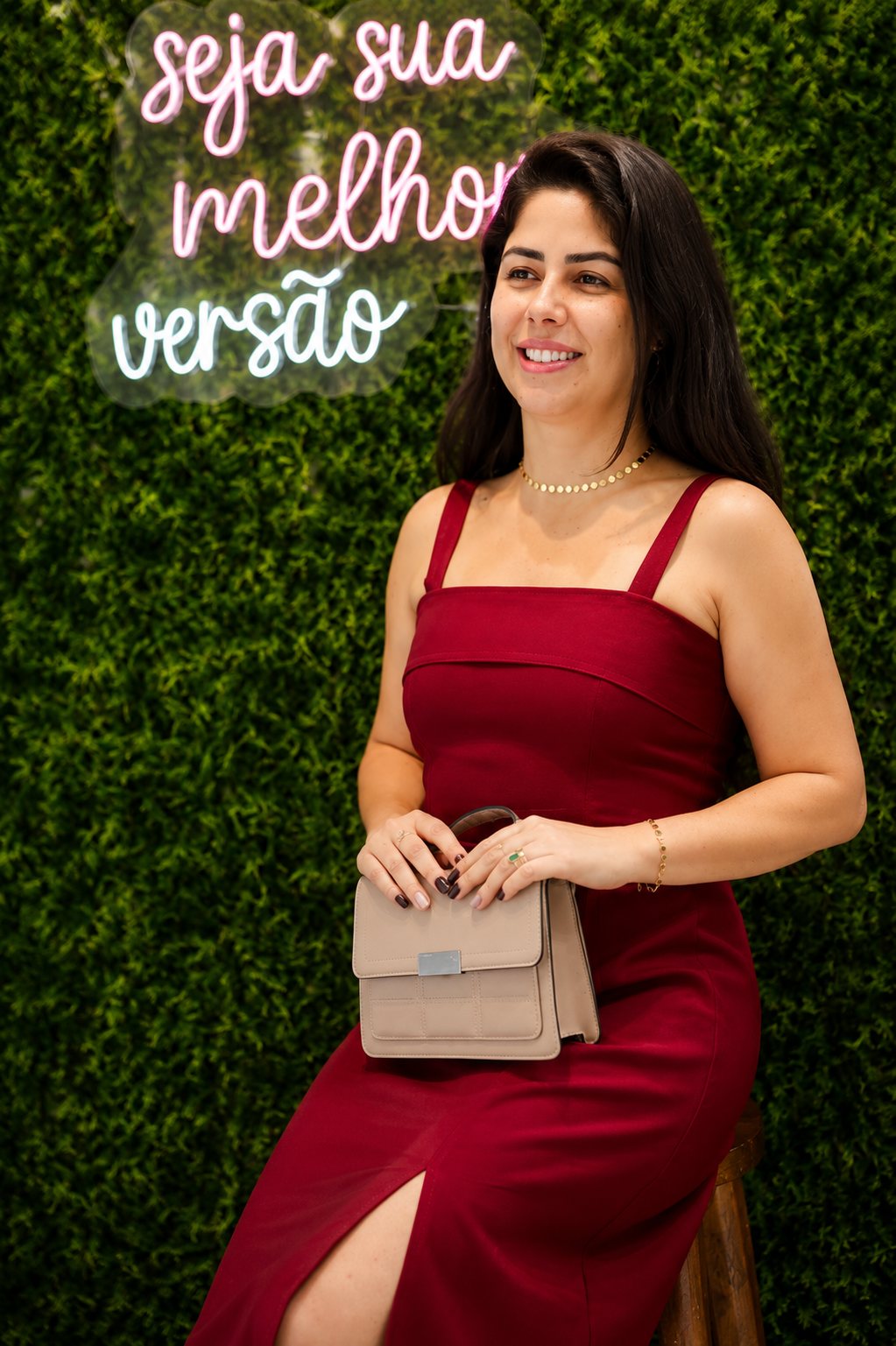 Aline usando um vestido bordô da Amara Belle, em frente ao painel 'seja sua melhor versão'.